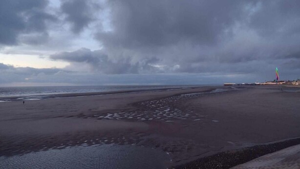 Una playa con un faro a lo lejos, bajo un cielo nublado.