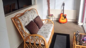 Una sala acogedora con un sofá de mimbre, una guitarra y una pequeña mesa con adornos.