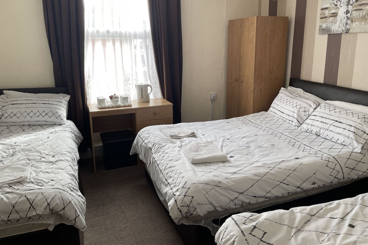 Een hotelkamer met twee bedden, een houten garderobe, een bureau met waterkoker en een schilderij aan de muur.