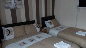 Habitación de hotel con dos camas, cada una con cabecero, mesita de noche y televisor de pared.