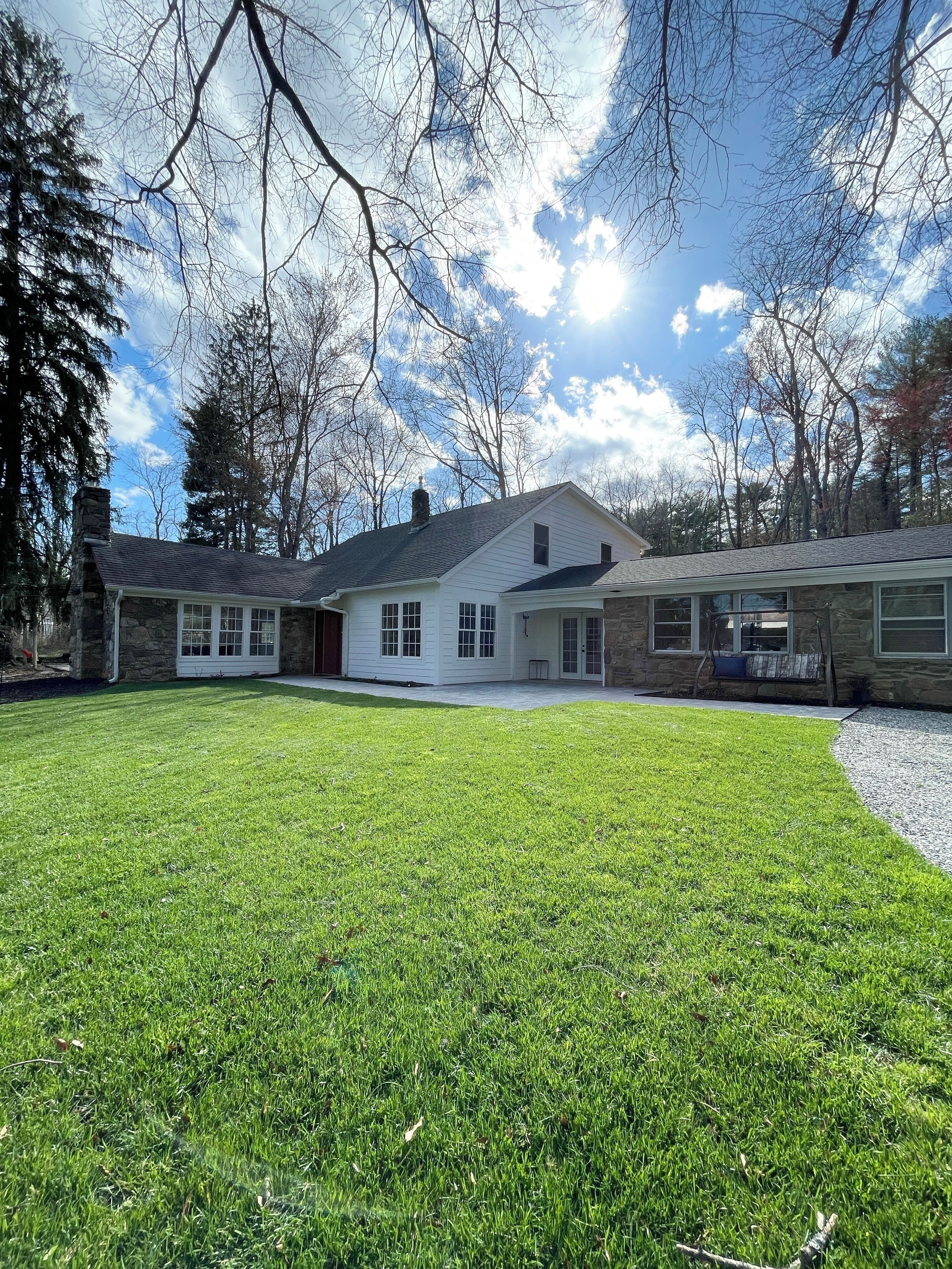 A two-story house with a stone chimney, a well-maintained lawn, and a clear sky.