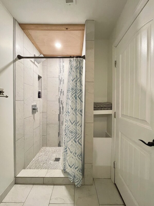 A small, enclosed shower area with a showerhead, a patterned shower curtain, and a tiled floor. - cozy family friendly home! Private Property! Minutes from Asheville downtown. (Asheville)