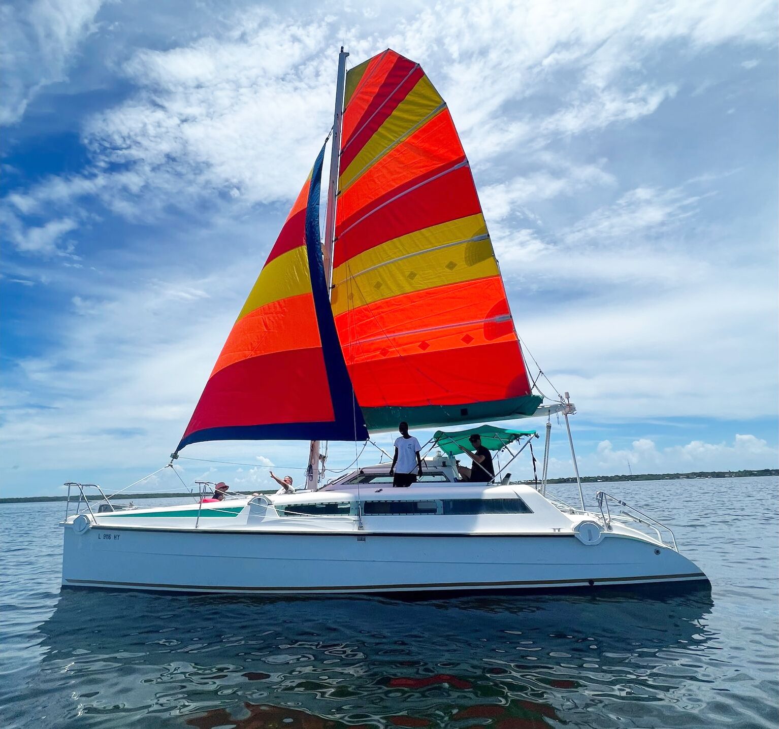 Un velero con una vela colorida, casco blanco y un mar tranquilo al fondo.