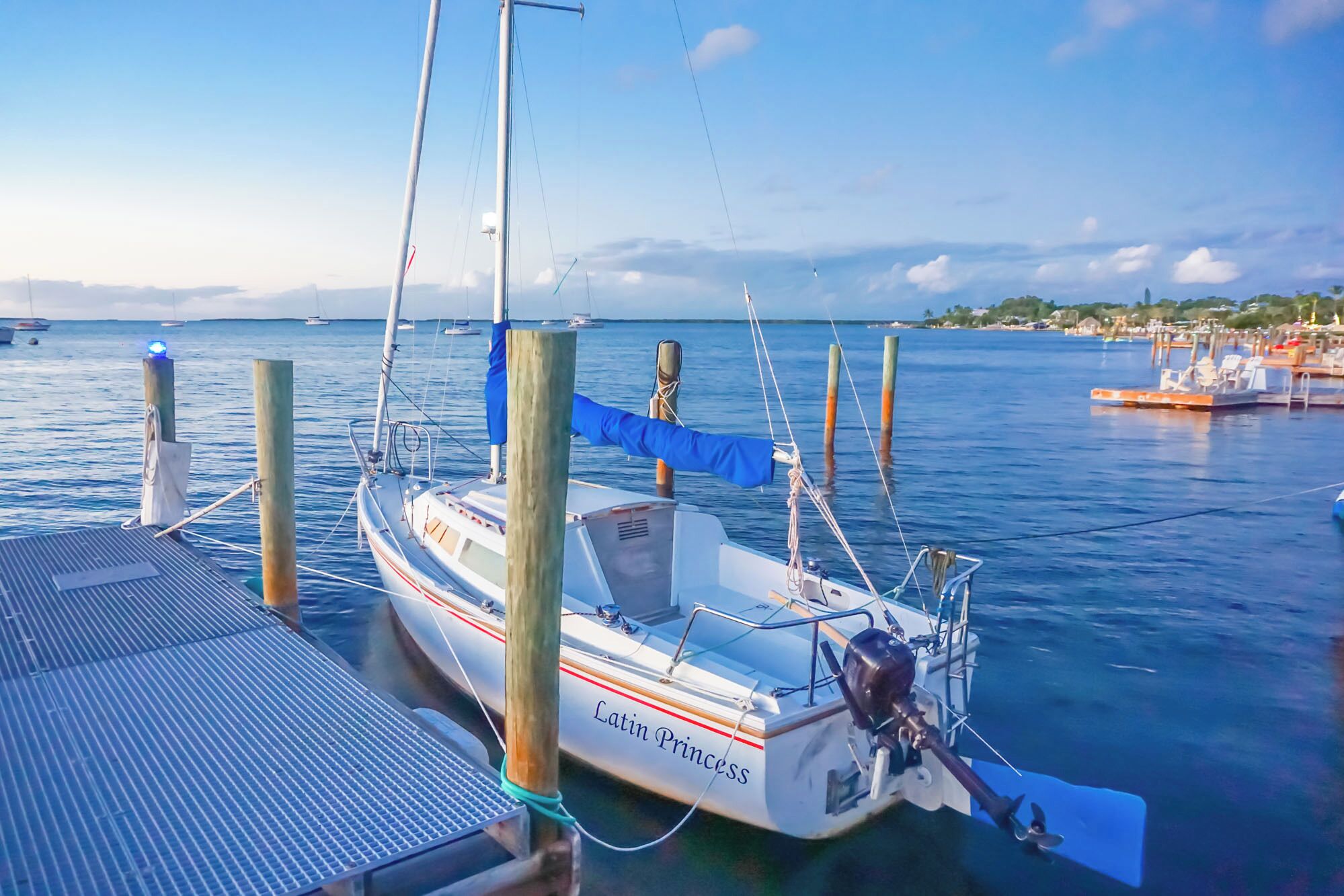 A sailboat named 'Latin Princess' docked at a pier with a clear view of the water and distant shoreline.