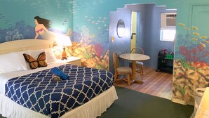 Une chambre comprenant un lit, une table et des chaises, décorée sur le thème du monde sous-marin, avec notamment une fresque représentant une sirène et des poissons.