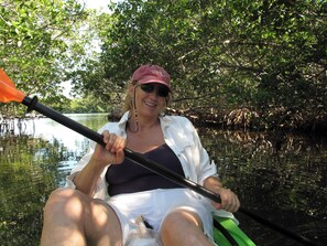 A person kayaking in a natural waterway surrounded by dense vegetation.