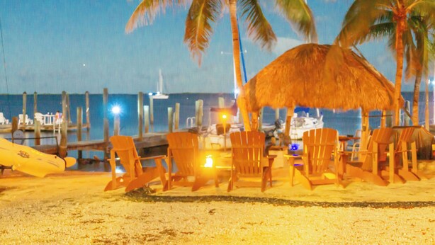 A beachside area with wooden chairs and a thatched-roof structure, likely a bar or seating area, overlooking the sea. - Bayside view Cottage , Free kayaks and sailboat (Key Largo)