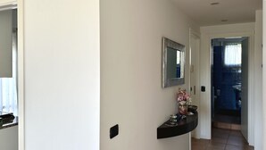 Un couloir avec un miroir, une petite étagère ornée d’objets décoratifs et une porte donnant sur une salle de bain.