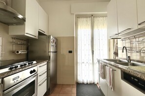 A compact kitchen with a stove, oven, refrigerator, and a window with curtains.