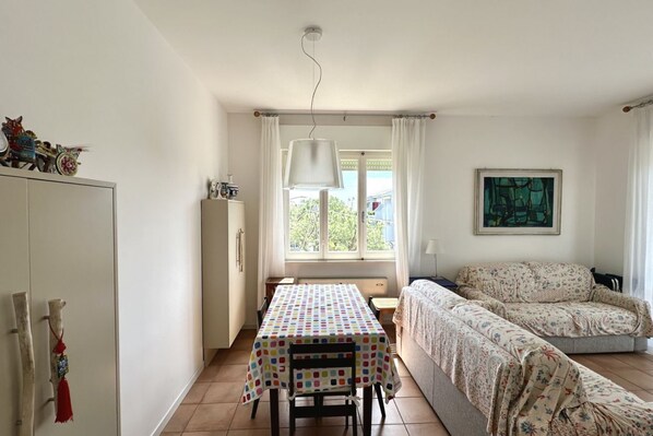 A room with a dining table, a sofa, a window with curtains, and a painting on the wall.