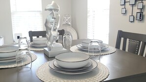 A dining table set with plates, bowls, and glasses, surrounded by chairs.