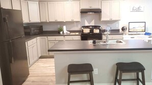 A modern kitchen with white cabinets, a black refrigerator, a stove, and a large island with two stools.