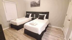 A hotel room with two single beds, a small desk, and a window with blinds.