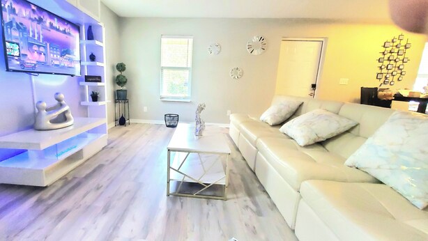 A modern living room with a flat-screen TV mounted on a white shelving unit, a white leather sofa, and a coffee table.