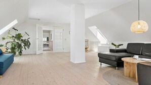 A spacious loft with high ceilings, a large skylight, a black leather sofa, a wooden coffee table, and a rattan pendant light.