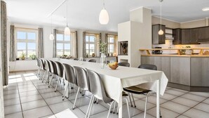 A modern dining area with a long table, multiple chairs, and pendant lighting.