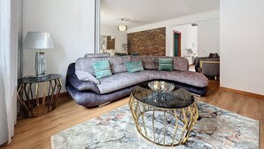 Un saló modern amb un sofà gris corbat, una taula de centre de vidre i una catifes amb dibuixos.