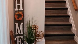 Una escalera con escalones de madera y barandilla, un cartel en la pared que dice 'HOME Sweet HOME' y una planta en maceta sobre un soporte de madera.
