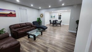 Una sala de estar moderna con un sofá de cuero marrón, una mesa de centro de vidrio y una zona de comedor con mesa y sillas.