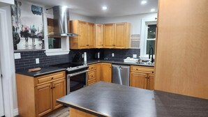 Cocina moderna con gabinetes de madera, extractor de acero inoxidable, lavavajillas y salpicadero de azulejos negros.