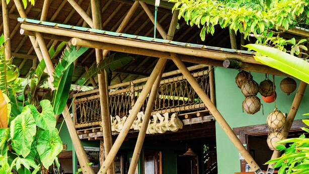 A rustic wooden structure with a thatched roof, stone pillars, and a dining area with wooden furniture. - ECOLODGE EL ALMEJAL (Bahia Solano)