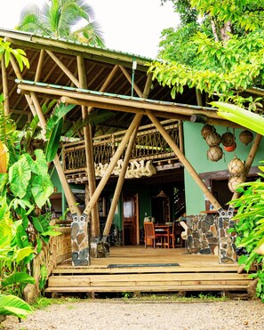 A rustic wooden structure with a thatched roof, stone pillars, and a dining area with wooden furniture. - ECOLODGE EL ALMEJAL (Bahia Solano)