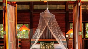 A wooden room with a bed under a canopy, stone walls, and a view of greenery outside. - ECOLODGE EL ALMEJAL (Bahia Solano)