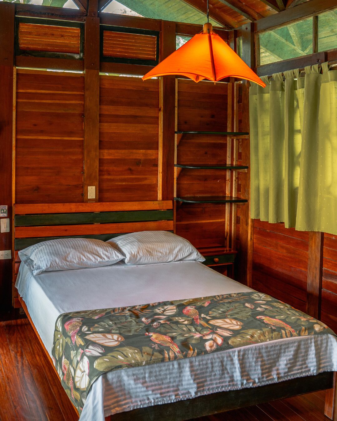A wooden room with a bed, a nightstand, and a hanging orange lamp.