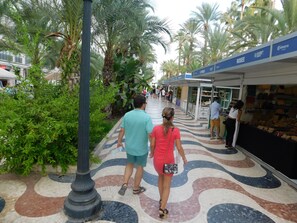 A tiled walkway with palm trees and a row of shops. - Bergantin Fantastic Sunny Apartment, Torrevieja, Communauté Valencienne, Espagne (Torrevieja)