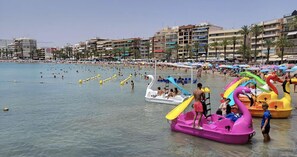 Une plage bondée, avec des bateaux gonflables et des parasols.