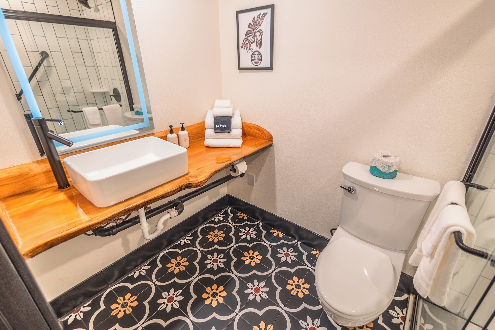 A bathroom with a wooden vanity, a white sink, a toilet, and patterned floor tiles.