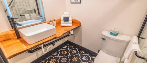 A bathroom with a wooden vanity, a white sink, a toilet, and patterned floor tiles.