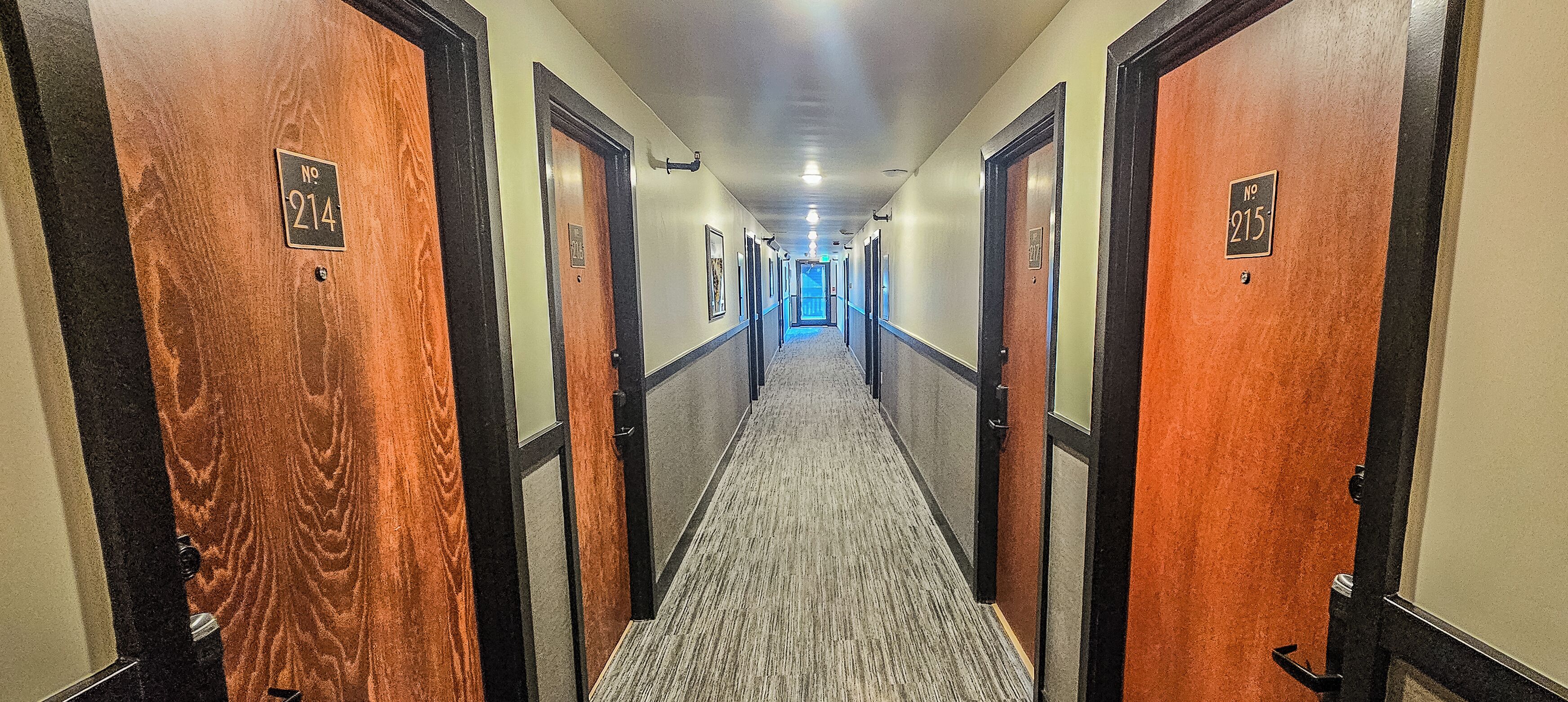 A hotel hallway with doors numbered 214 and 215, carpeted floors, and a light-colored wall.