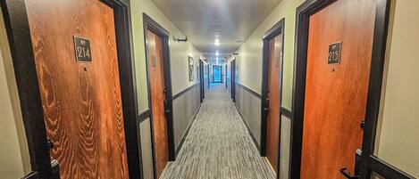 A hotel hallway with doors numbered 214 and 215, carpeted floors, and a light-colored wall.