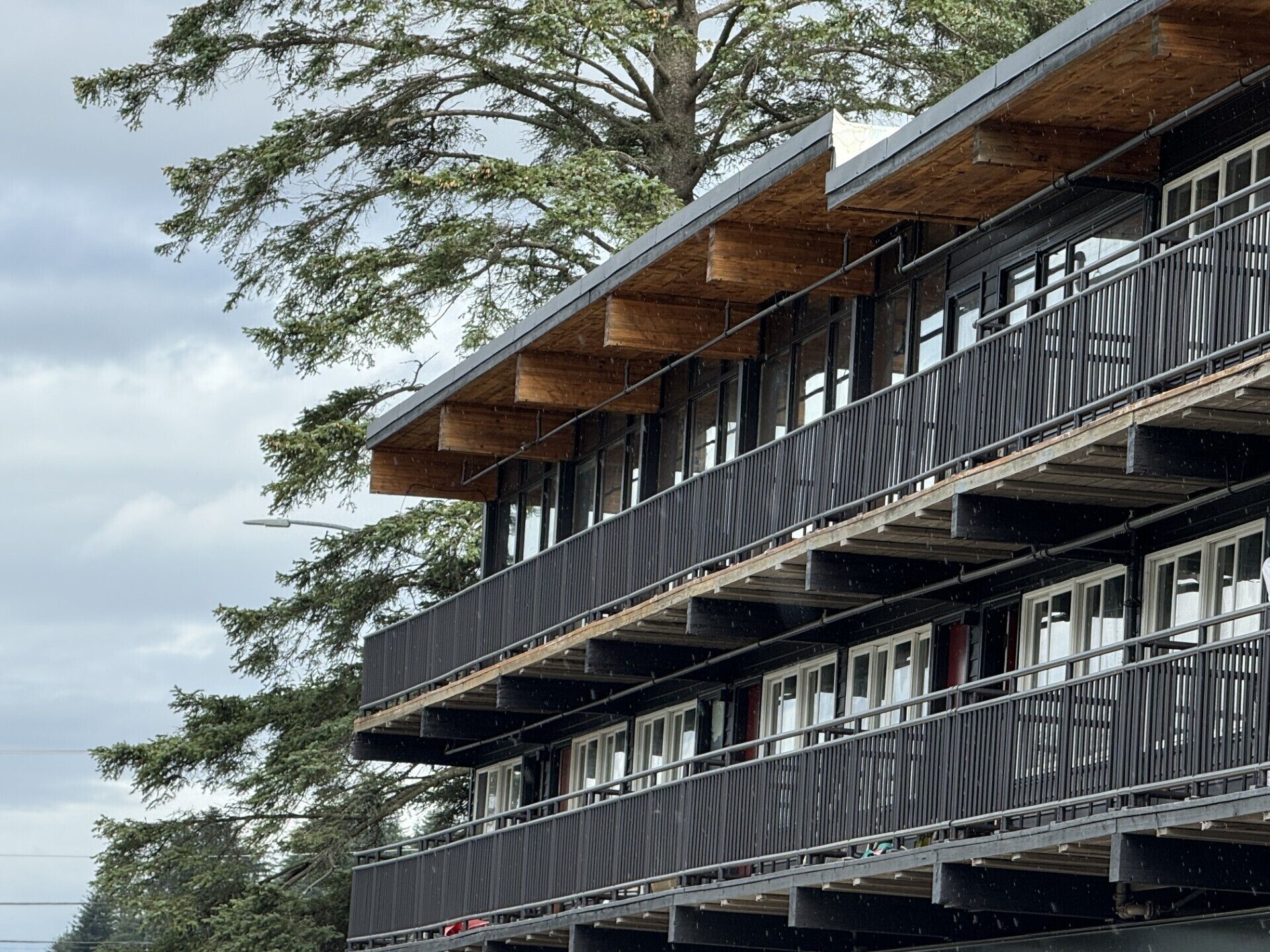 A multi-story building with balconies, large windows, and a wooden upper floor.