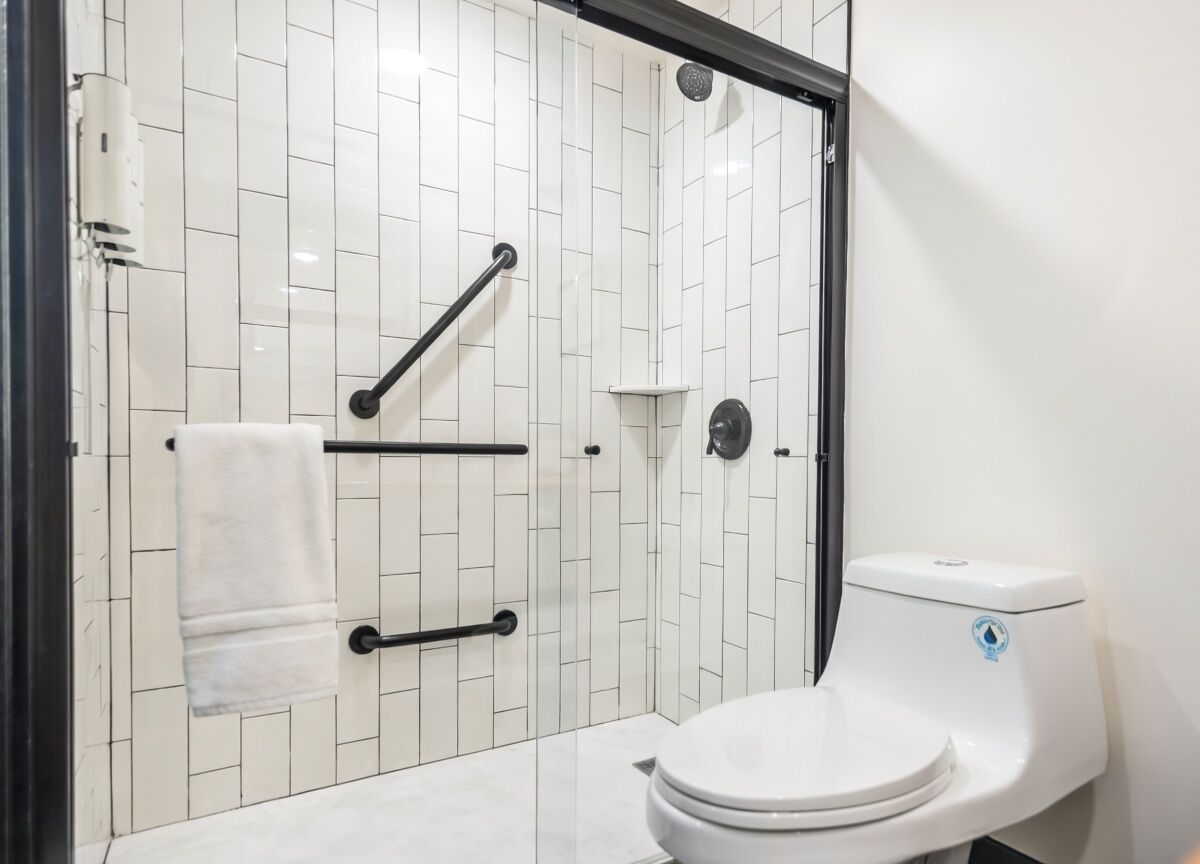 Un baño moderno con paredes de azulejos blancos, un inodoro blanco, cabina de ducha de cristal y un perchero para toallas.
