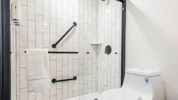 Un baño moderno con paredes de azulejos blancos, un inodoro blanco, cabina de ducha de cristal y un perchero para toallas.