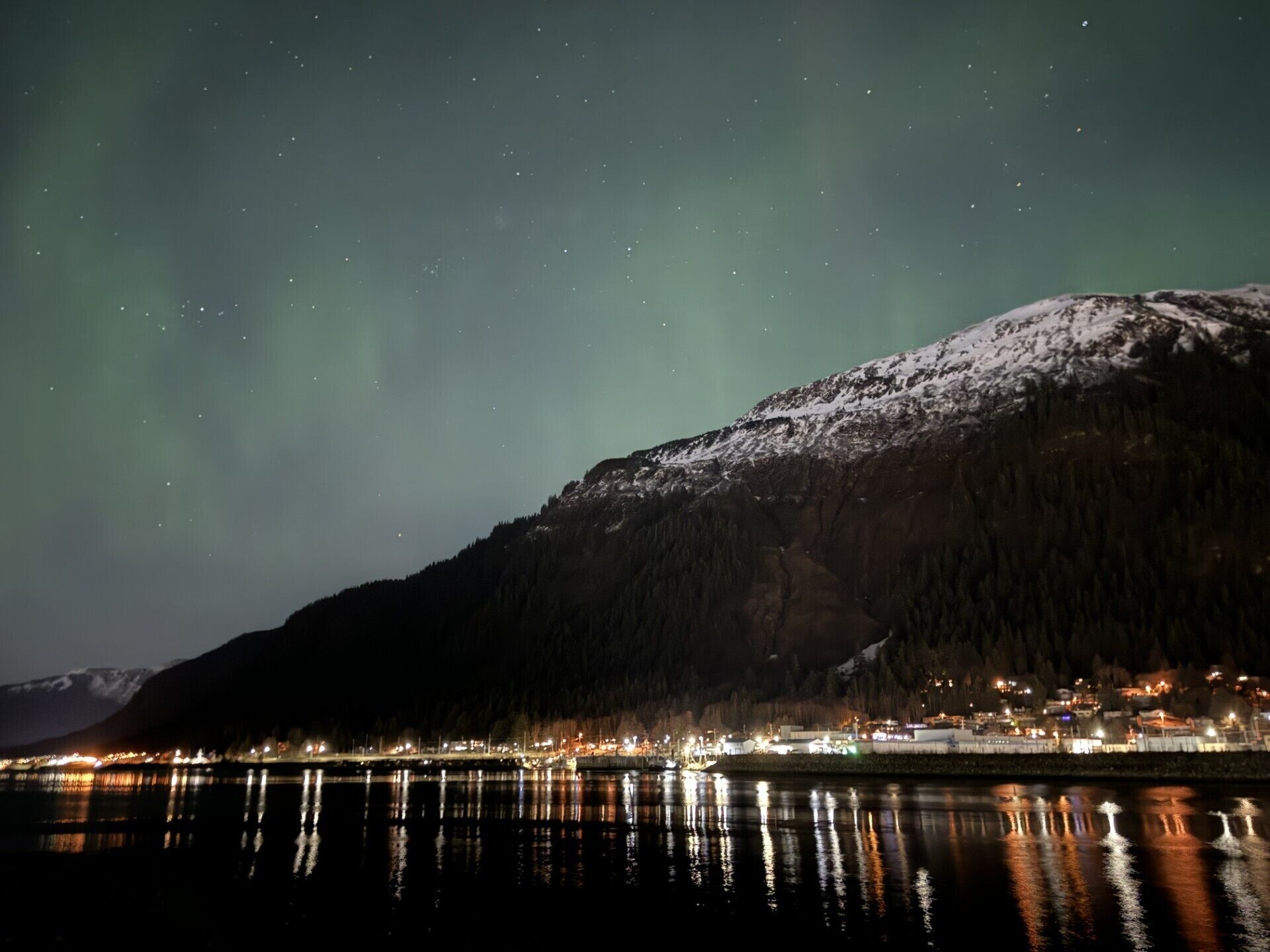 A night view of a snow-covered mountain with a town in the foreground.