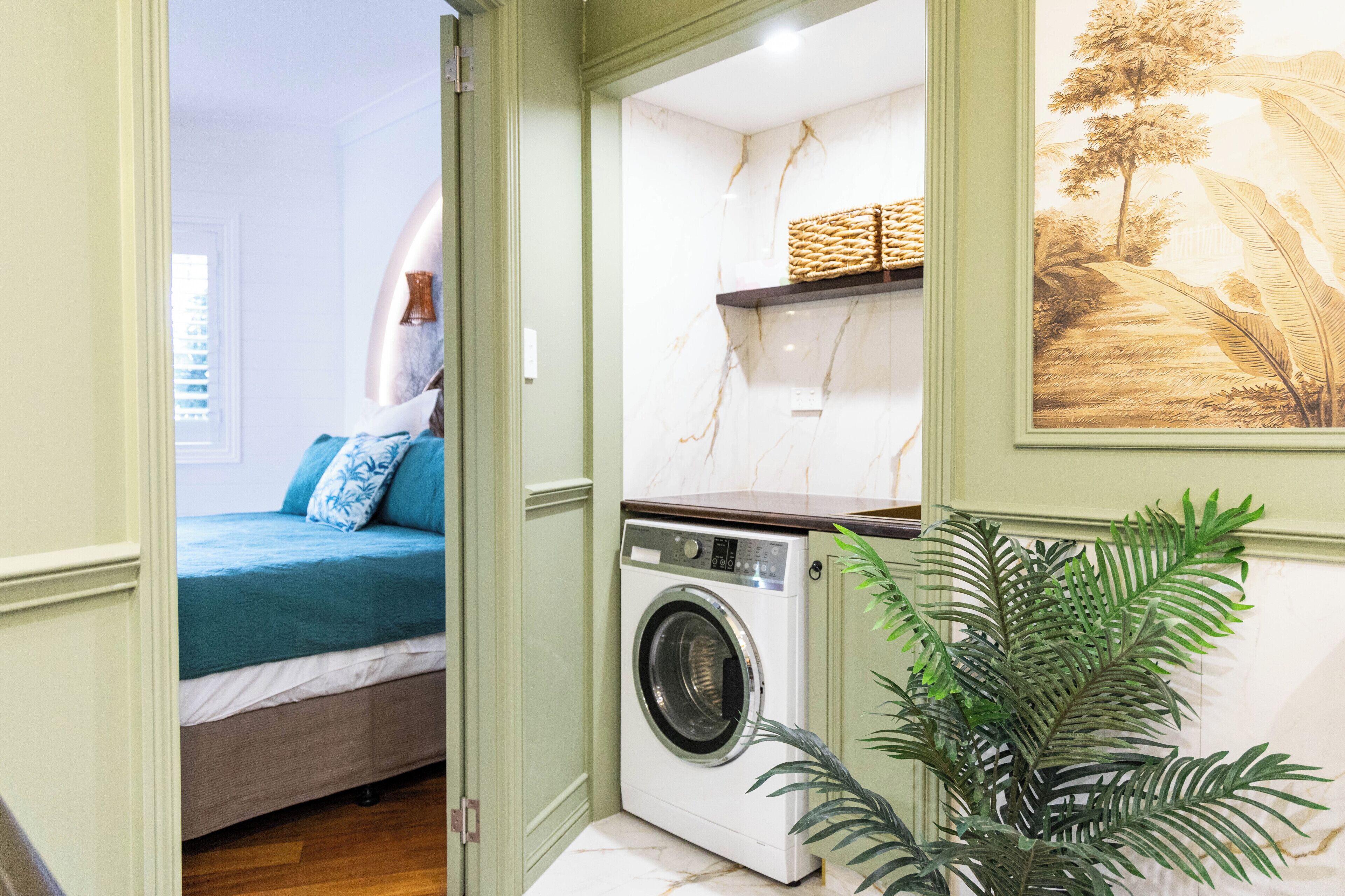 A compact room with a bed, a washing machine, and a plant.