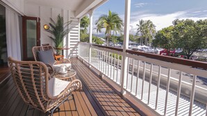 Un balcone con mobili in vimini, una ventola a soffitto e vista su un’area di parcheggio con palme.