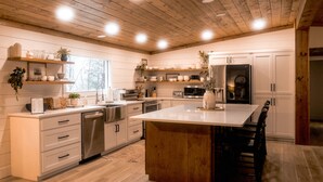 Una cocina moderna con techo de madera, muebles blancos y electrodomésticos de acero inoxidable.