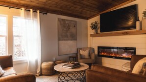 Un salón acogedor con chimenea, asientos cómodos y un televisor grande en la pared.
