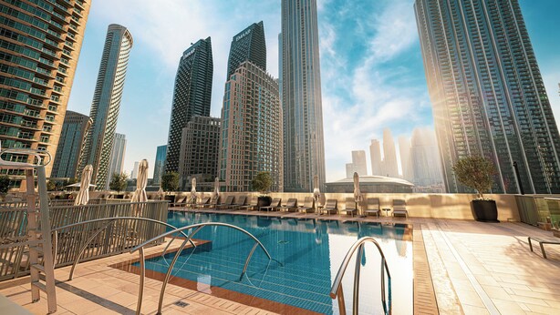 Un área de piscina en la azotea con vistas a edificios altos, incluyendo un rascacielos destacado con el nombre 'EMAR'.