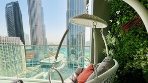 Una silla colgante con cojín, barandilla de vidrio y vista panorámica de un paisaje urbano con edificios altos.
