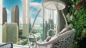 Una silla de mimbre blanca con cojín, con vistas a un paisaje urbano con edificios altos y una pared verde con plantas.