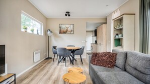 Un soggiorno moderno con un divano grigio, un tavolo da pranzo con sedie, una TV su un mobile basso e una cucina sullo sfondo.
