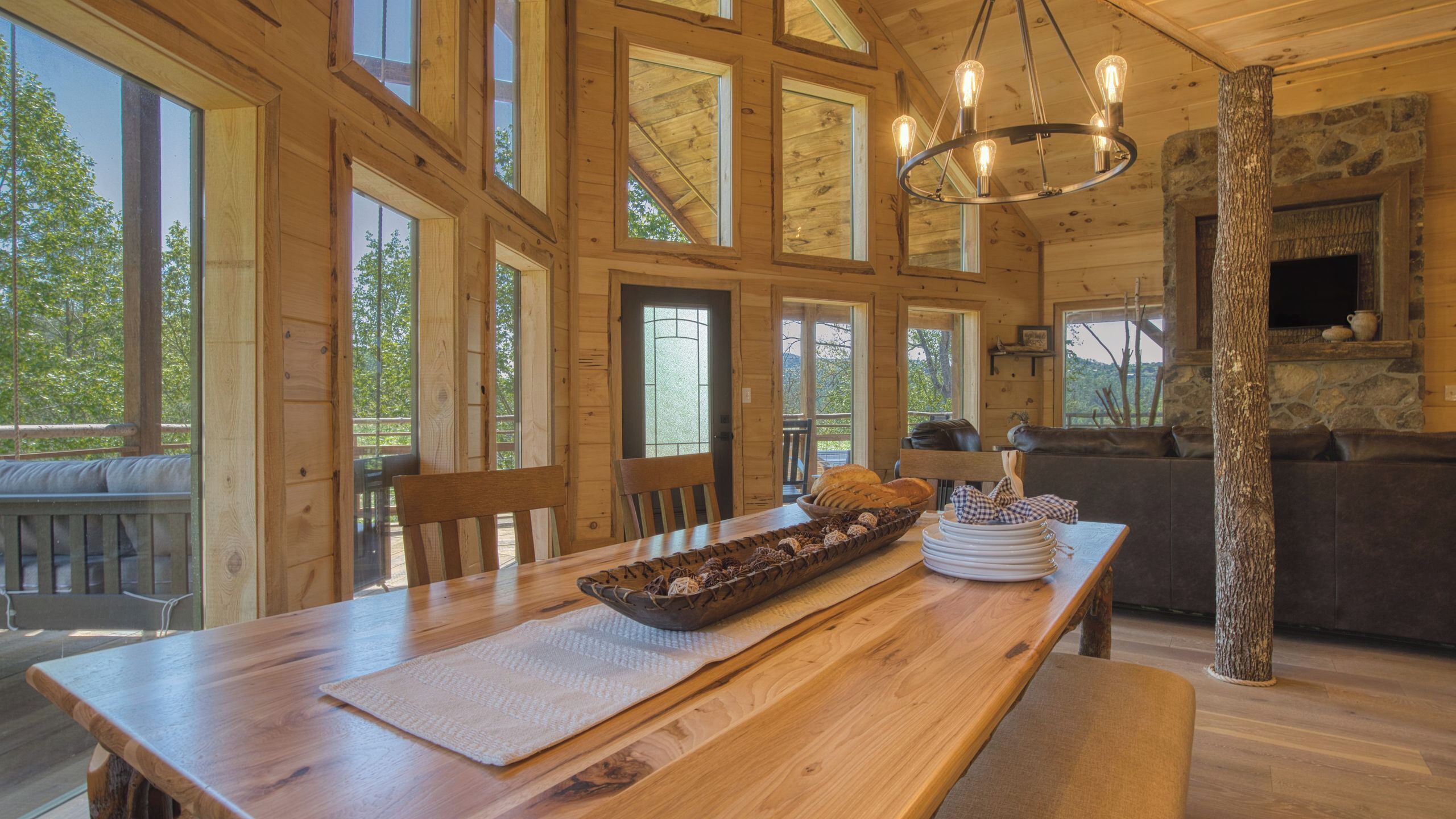 Ein Holzblockhaus-Interieur mit Esstisch, Stühlen, Kamin und großen Fenstern.