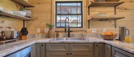 A kitchen with wooden walls, a granite countertop, a sink, and various kitchen items.