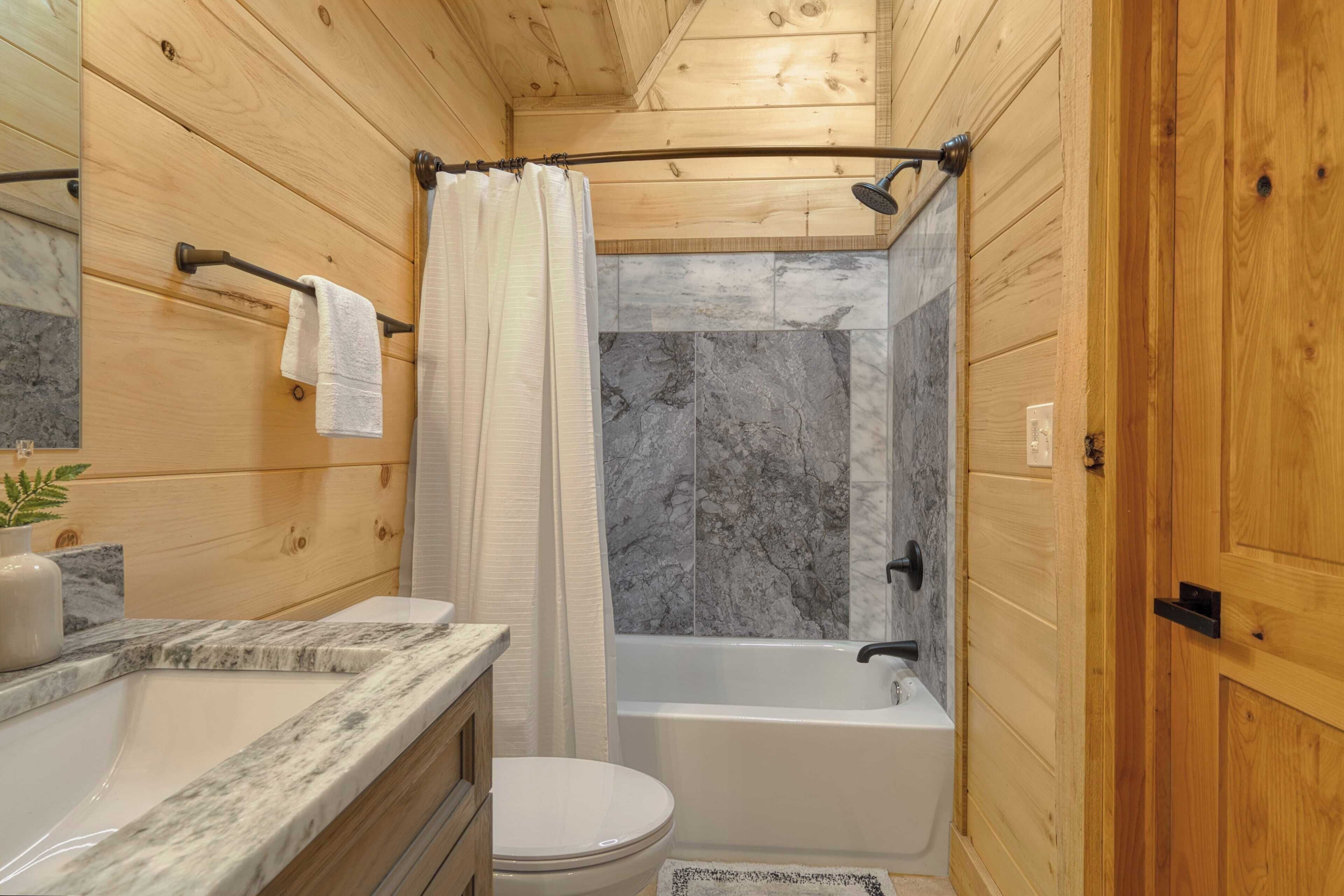 Une salle de bain avec des murs en bois, un comptoir en marbre, des toilettes, une baignoire et un rideau de douche.