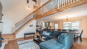 Ein geräumiges Wohnzimmer mit einem großen, blauen Ecksofa, einer Holztreppe und einer Küche im Hintergrund.